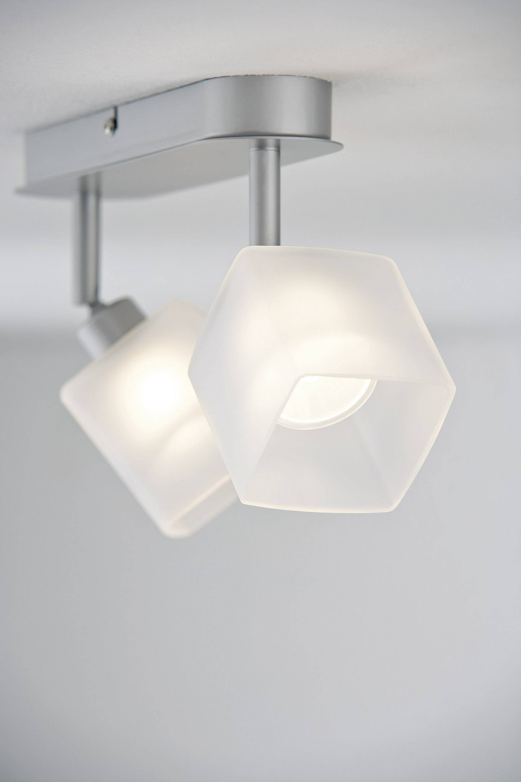 Deux luminaires hexagonaux montés au plafond, dotés d'abat-jours en verre blanc mat, diffusant une lumière douce et diffuse dans la pièce.