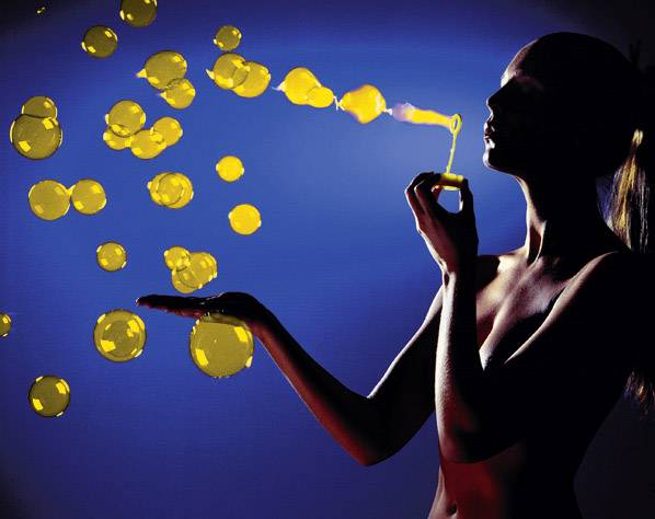 Une personne souffle des bulles de savon jaune lumineux contre un fond bleu, avec quelques bulles flottant dans sa main.