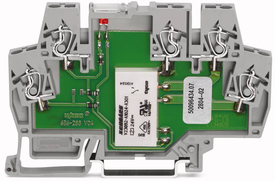 Un composant avec un circuit imprimé vert et des relais blancs dans un boîtier gris ; c'est un dispositif électrotechnique.