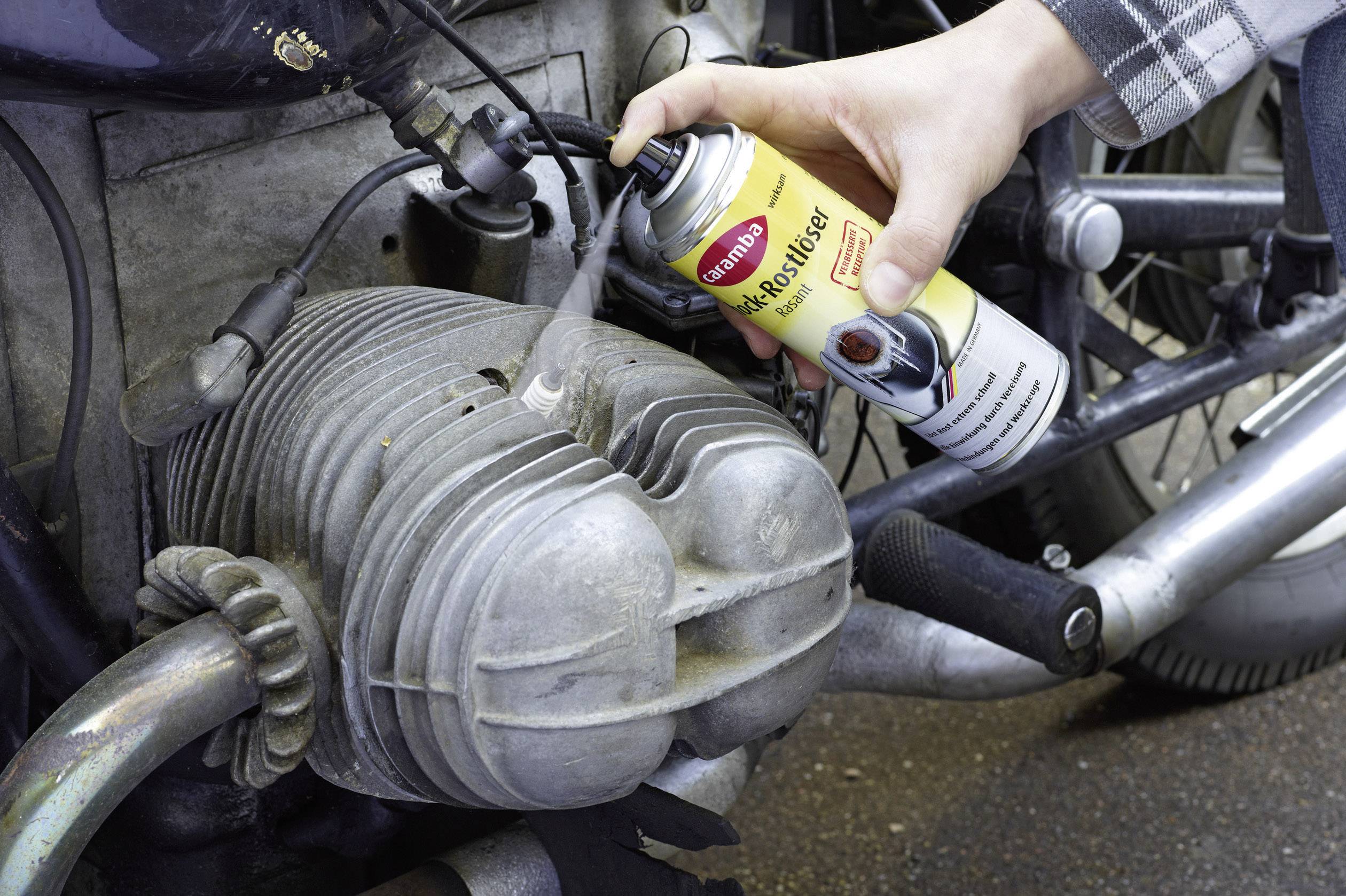 Une main nettoie une pièce de moto avec un spray moteur en bombe