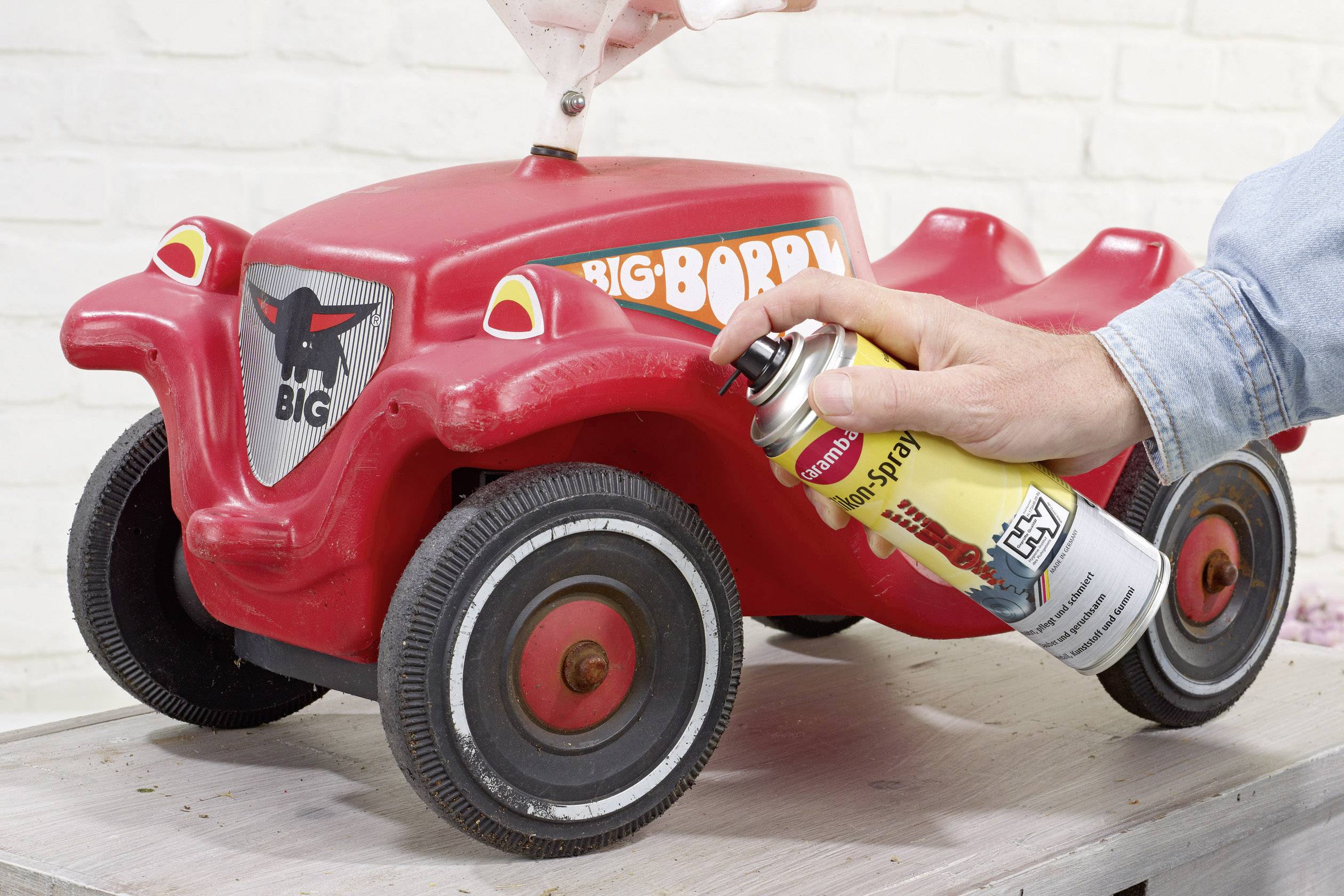 Une voiture Bobby-Car rouge est scellée avec une bombe aérosol. Une personne tient la bombe et pulvérise sur le véhicule.
