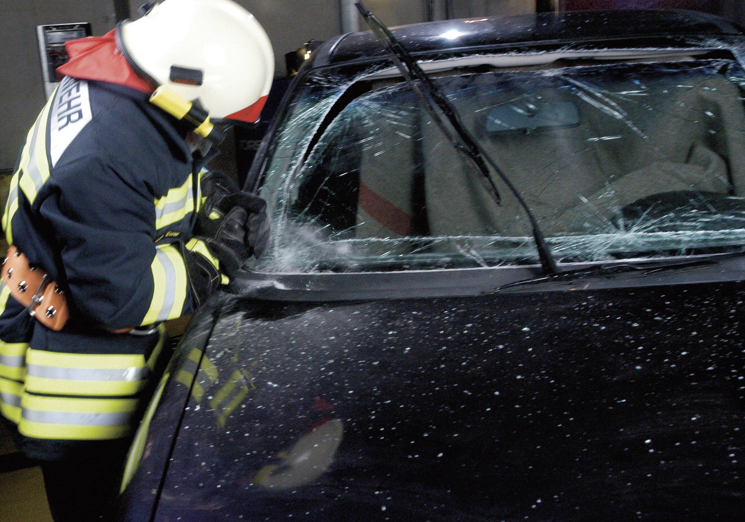 Un pompier brise la vitre avant fêlée d'une voiture noire lors d'une intervention de secours.
