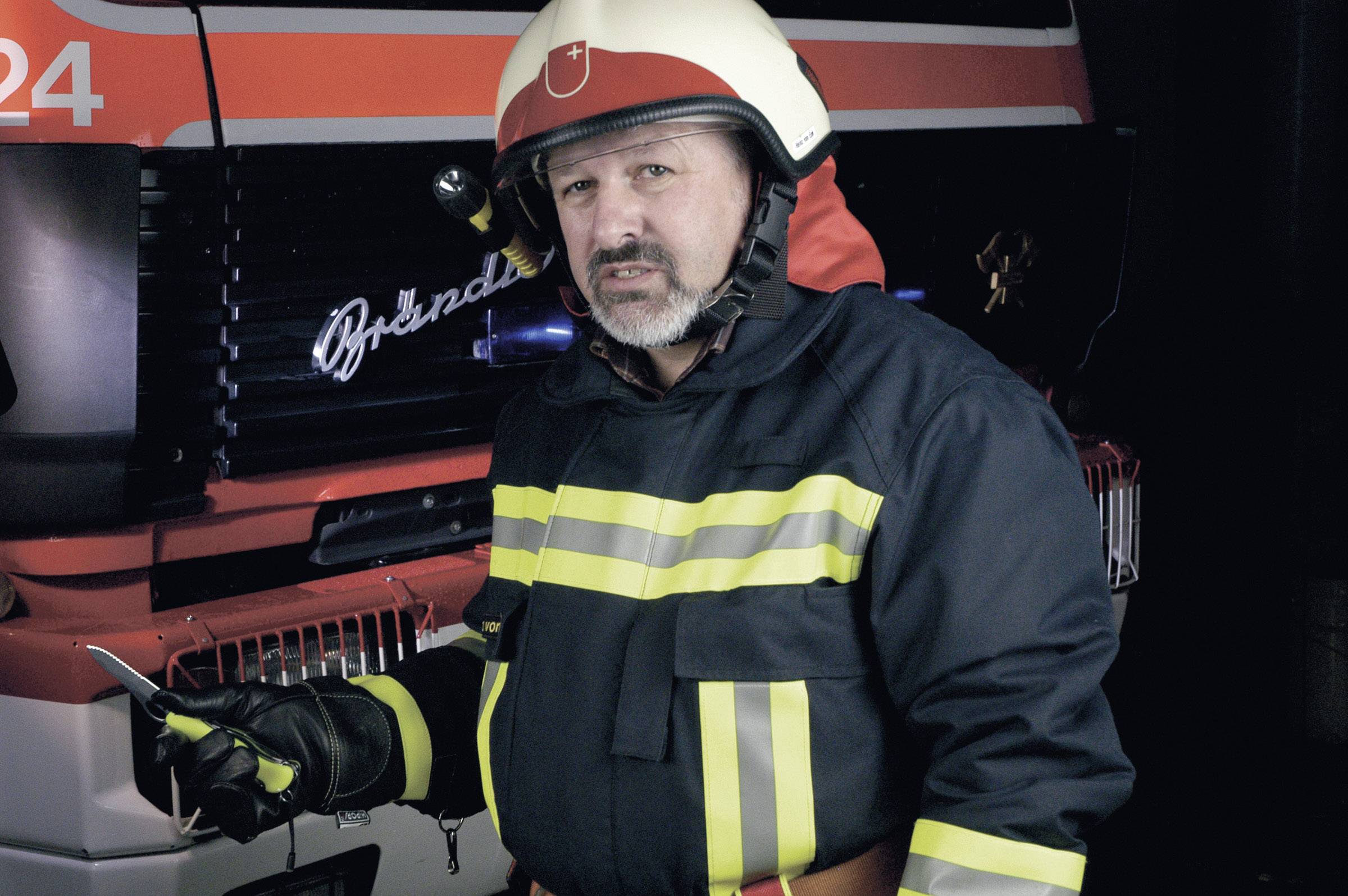 Un pompier en tenue complète se tient devant un camion de pompiers et tient une radio.