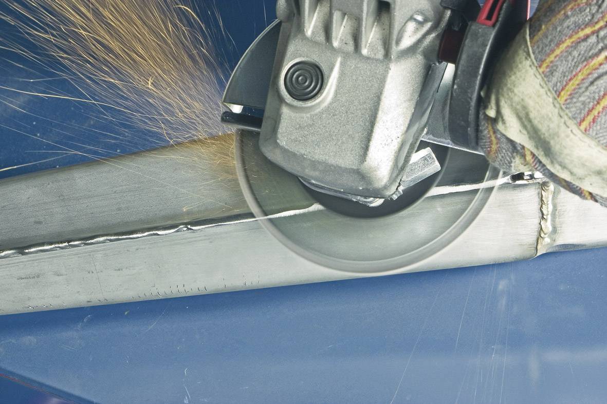 Une meuleuse traite une poutre métallique, des étincelles se produisent. Une main gantée de gants de travail maintient fermement la machine.