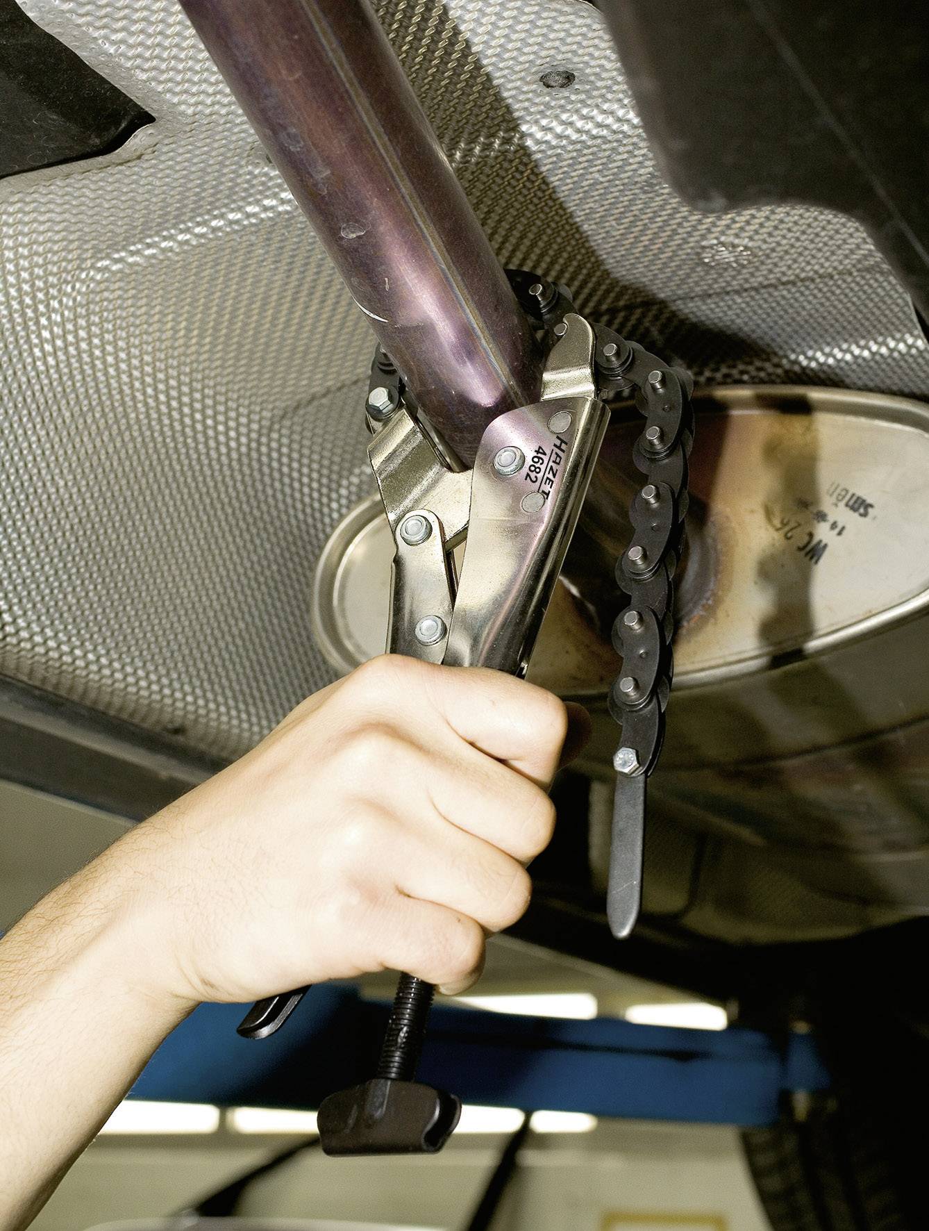 Une main utilise un coupe-tube pour couper un tuyau métallique, probablement lors d'une réparation ou d'une installation.