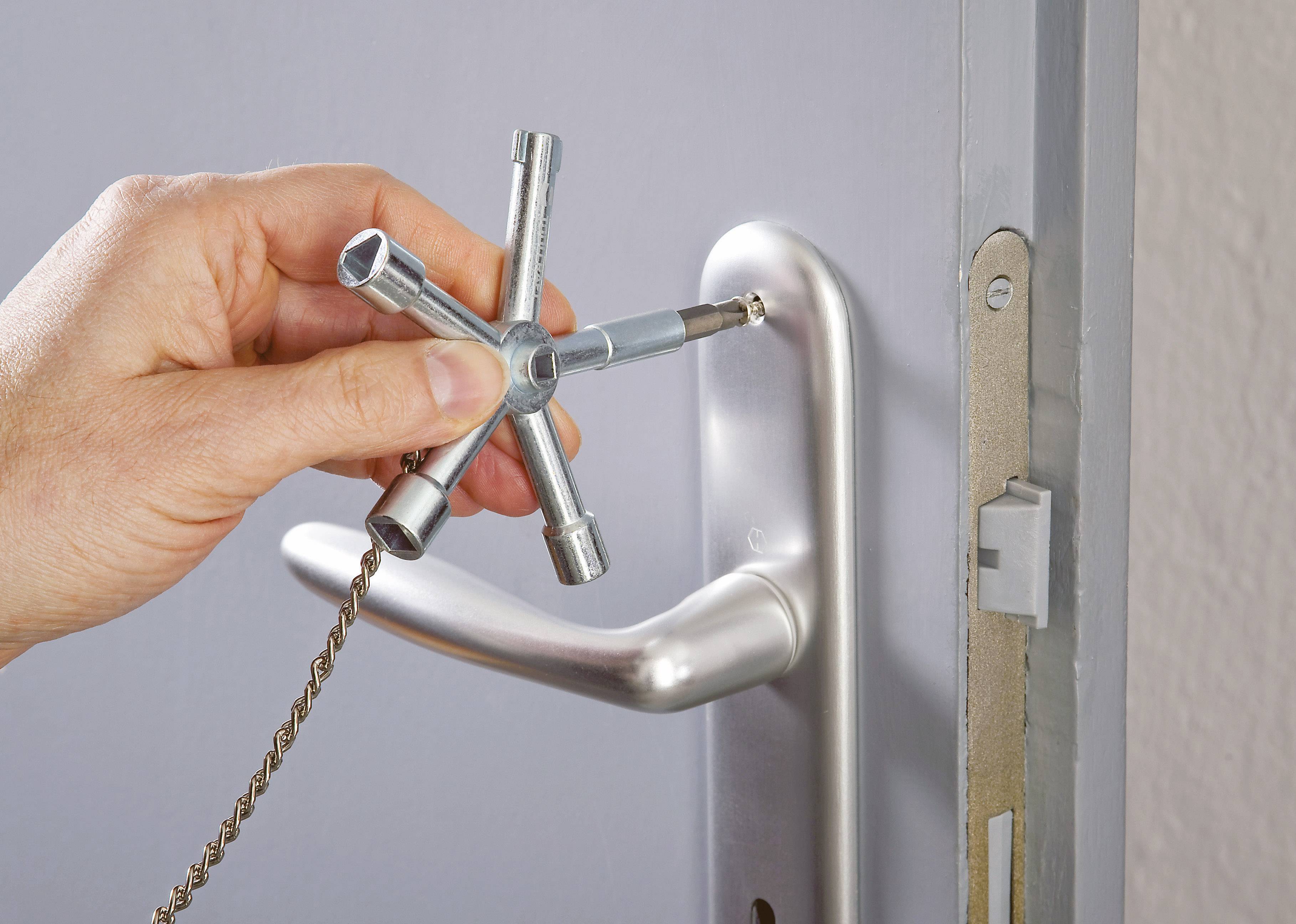 Une personne répare une serrure avec une clé universelle. La clé possède plusieurs branches et est positionnée sur la poignée de la porte.