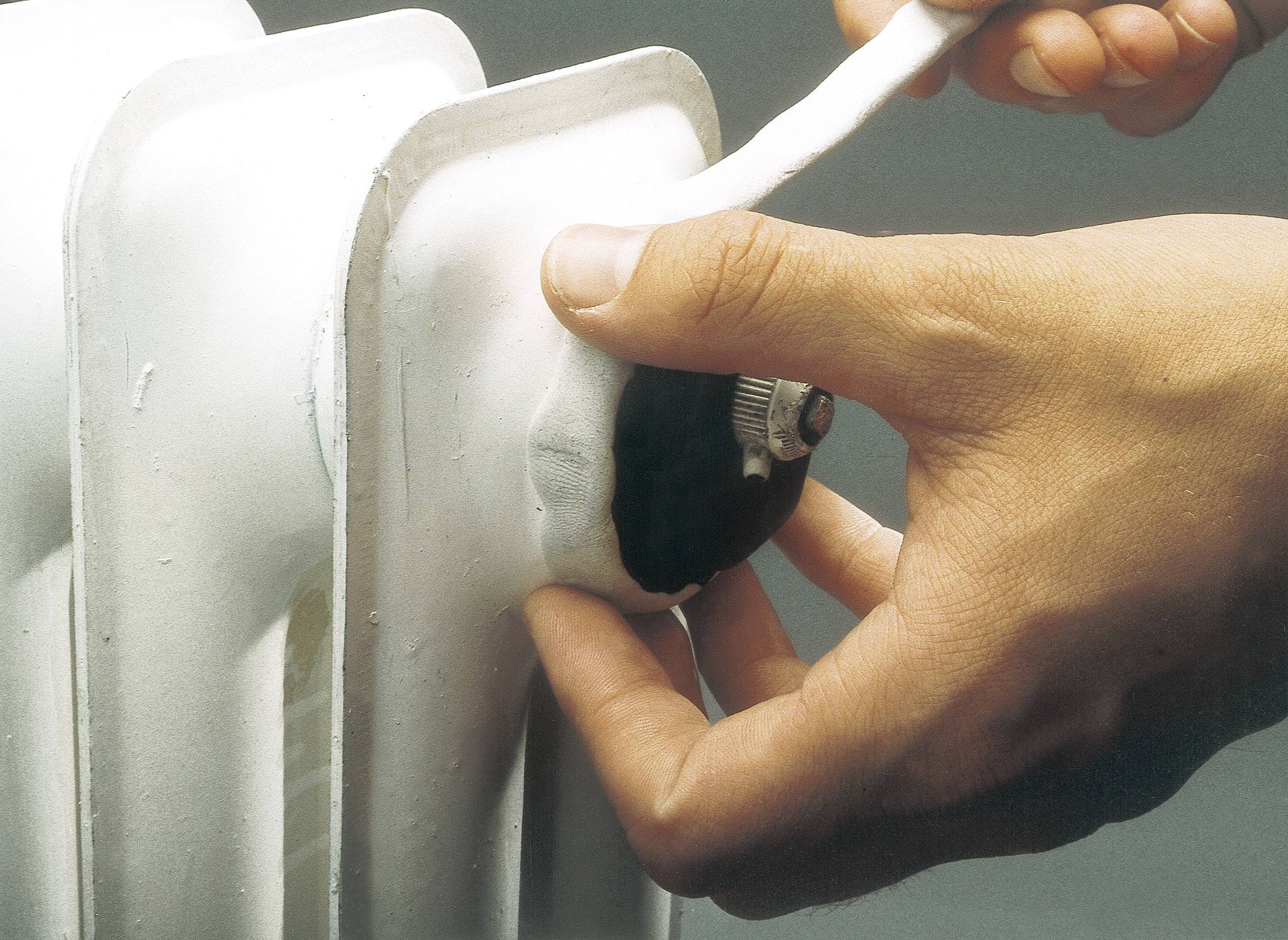 Une main tourne une vanne sur un radiateur blanc. Une autre main tient un matériau isolant.