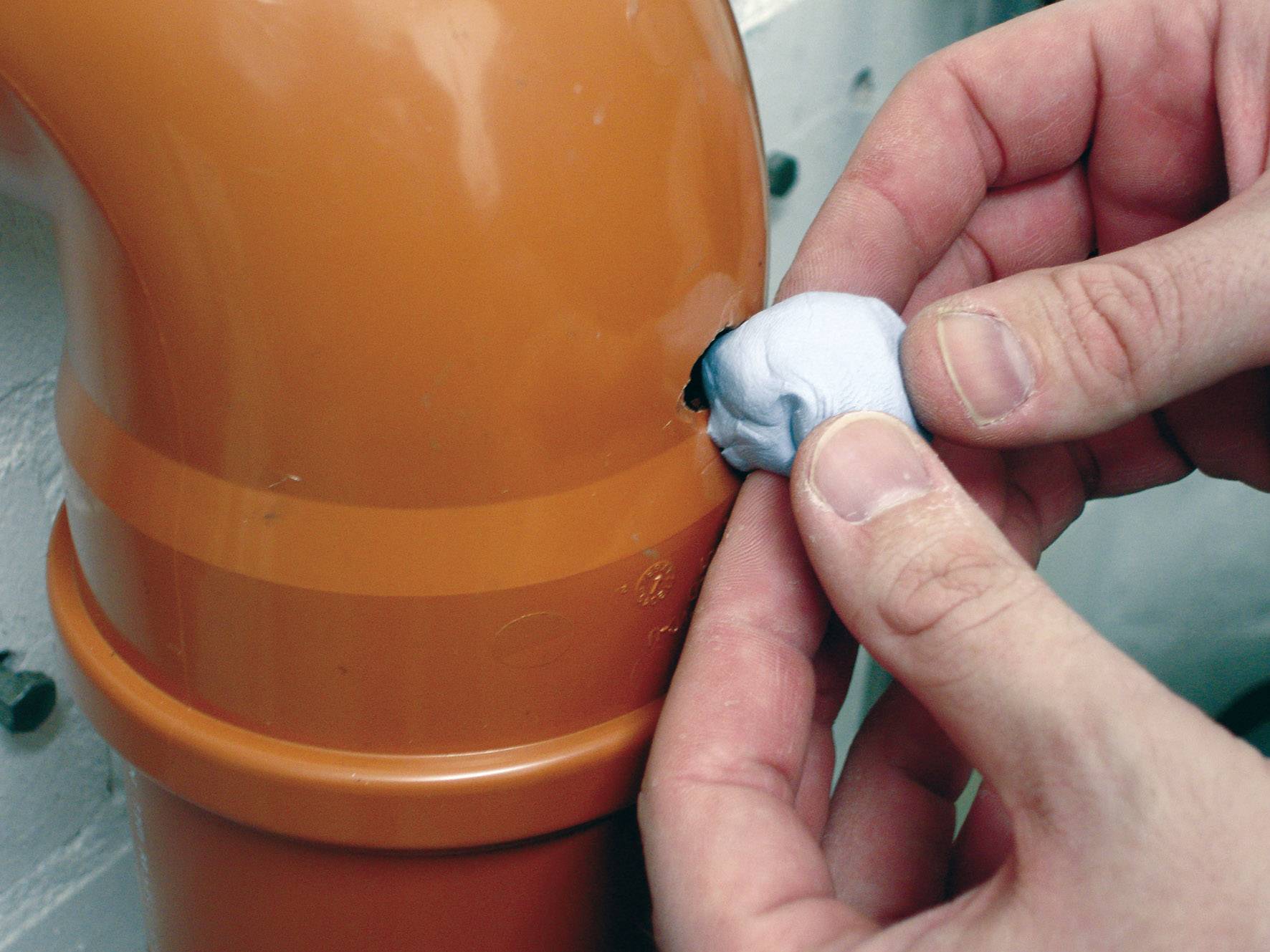 Une personne répare un petit trou dans un tuyau orange à l'aide d'une pâte à modeler bleue afin de prévenir une fuite.