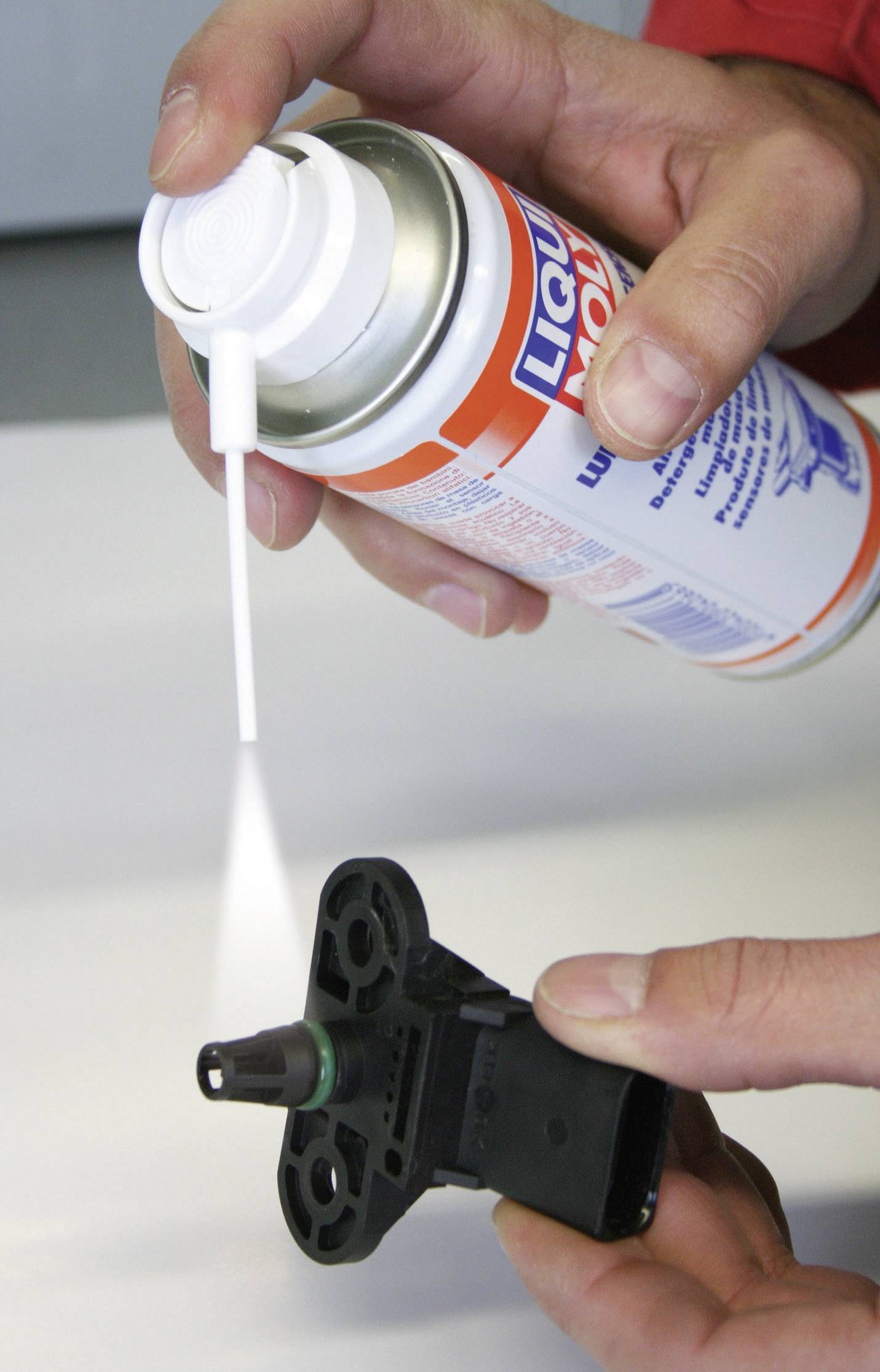 Une personne vaporise un produit nettoyant d'un aérosol sur un petit capteur noir. Le capteur est tenu à la main.