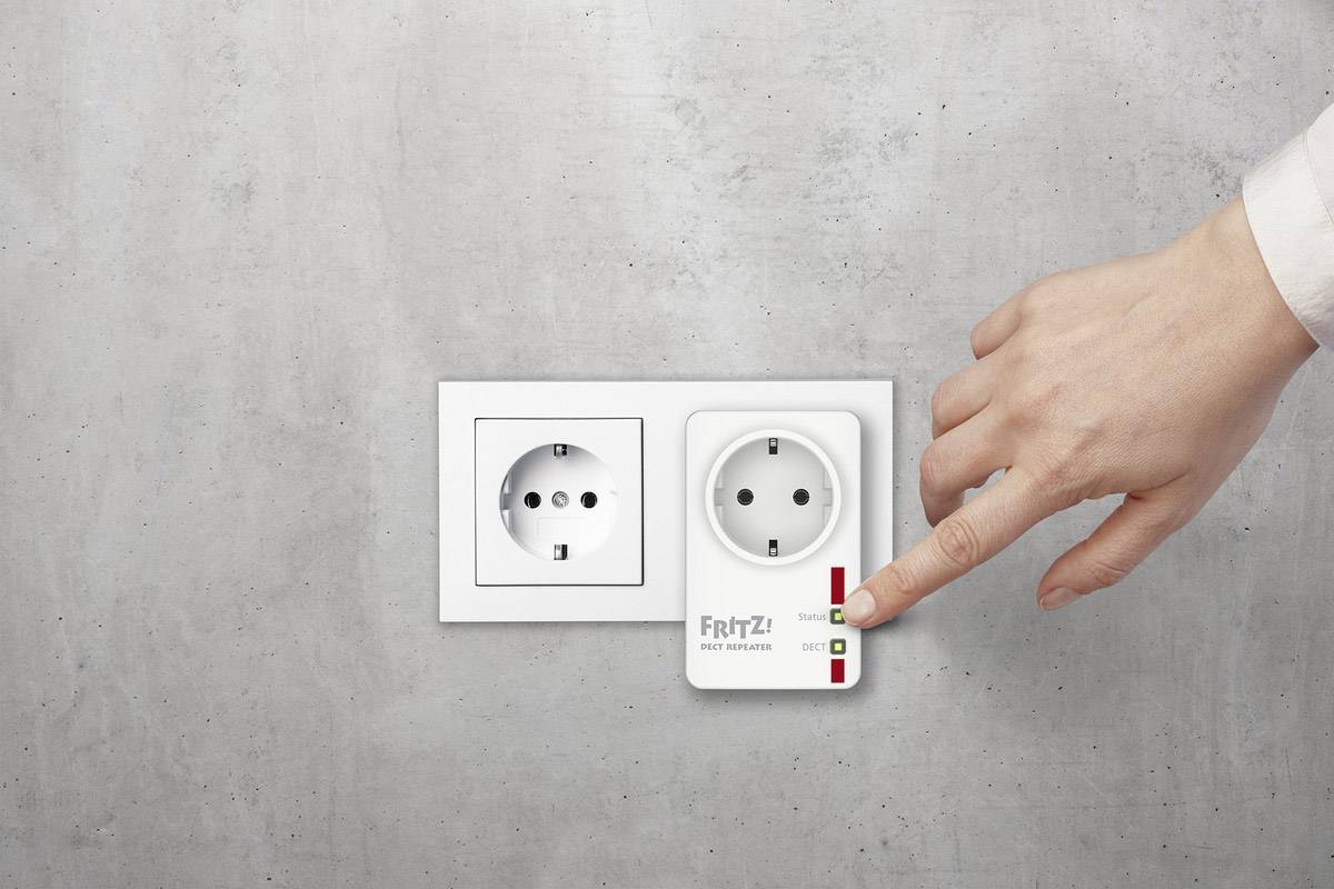 Une main manipule une prise intermédiaire 'FRITZ! DECT 200' branchée dans une prise murale. La prise est allumée.